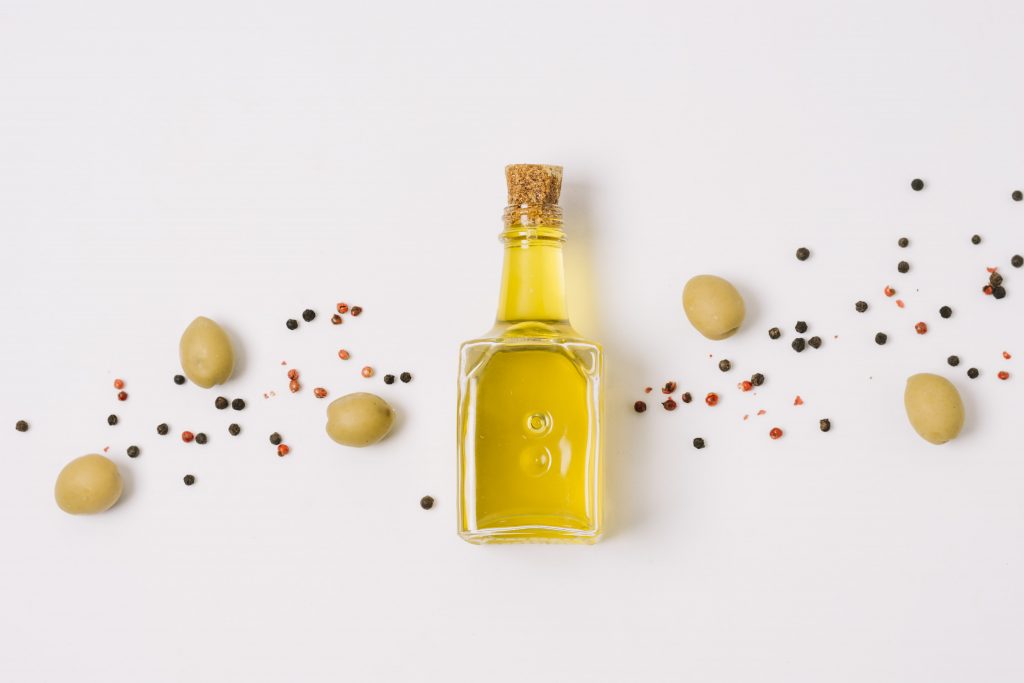 Imagen en que se muestra una botella de aceite de oliva, ornamentada con olivas a su alrededor. 