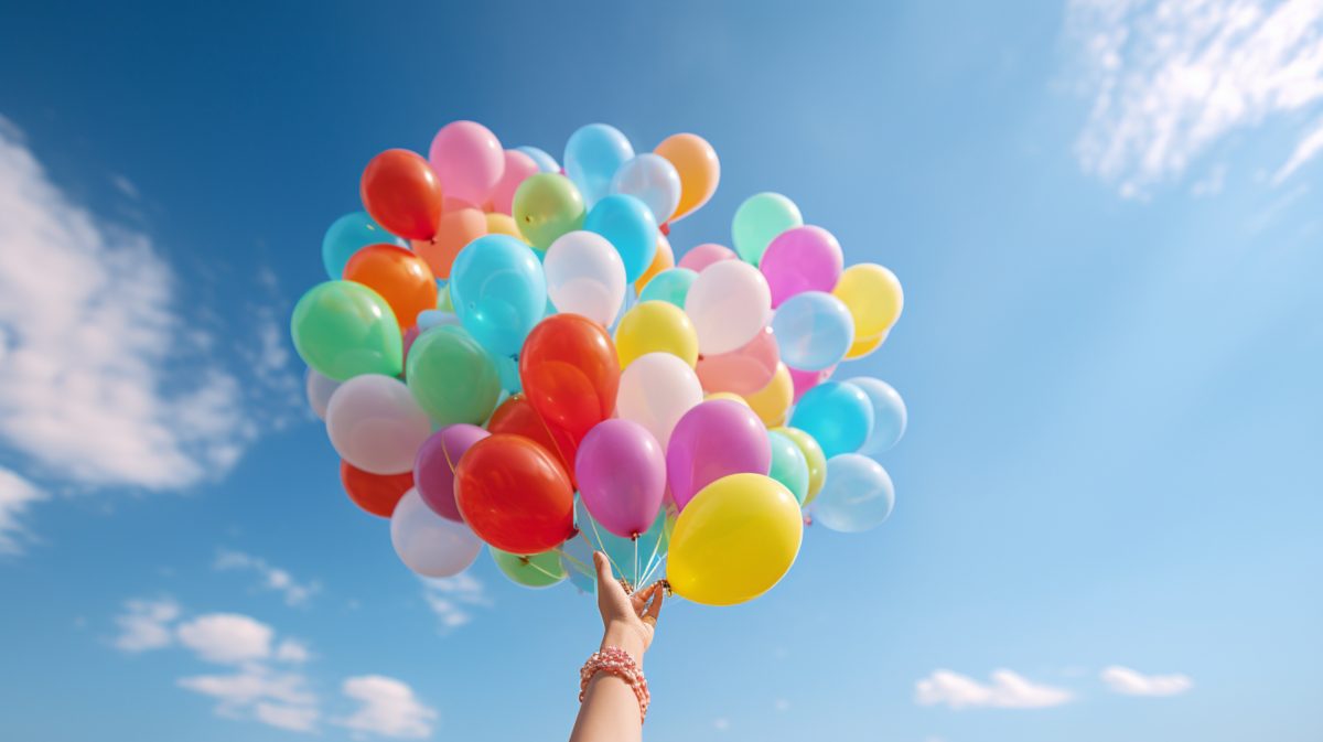 Una mano suelta un ramo de globos de helio al cielo